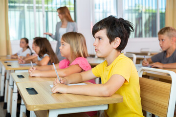 Sad bored schoolboy sitting in classroom during lesson in elementary school