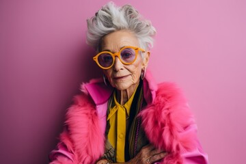 Fashionable senior woman in pink jacket and sunglasses on pink background