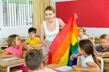 Positive female teacher standing with lgbt flag, supporting diversity in school during lesson