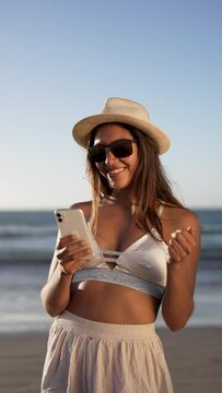 portrait young smiling latin american woman holding and looking a cellphone on the beach