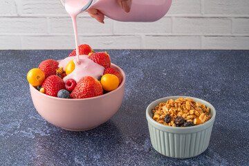 Hand pouring yogurt to a bowl with seasonal fruit