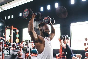 Energetic black man exercising with dumbbells in gym