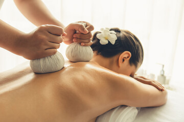 Hot herbal ball spa massage body treatment, masseur gently compresses herb bag on woman body. Tranquil and serenity of aromatherapy recreation in day lighting ambient at spa salon. Quiescent