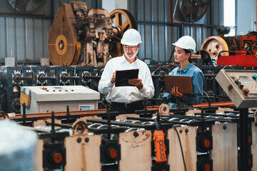 Factory engineer manager with assistant using laptop to conduct inspection of steel industrial machine, exemplifying leadership as machinery engineering inspection supervisor in metalwork manufacture. - obrazy, fototapety, plakaty