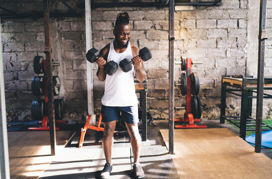 Positive ethnic sportsman exercising with dumbbells