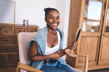 Cheerful black woman with mirror sitting on armchair