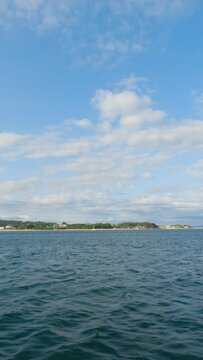 Coroso Beach in Santa Ux&iacute;a de Ribeira. Slow-motion of the azure sea, revealing the coastline with houses and distant lush mountains under a summer sky adorned with wispy clouds.