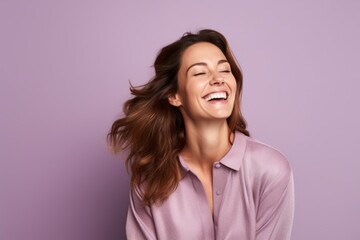 Portrait of a happy young woman with closed eyes, laughing and looking at the camera on a purple background