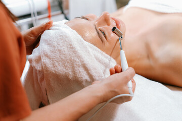 Beautiful caucasian woman lying on spa bed during having facial massage by professional hands at modern spa salon surrounded by beauty electrical equipment or medical equipment. Close up. Tranquility