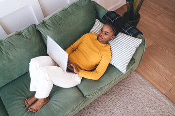 Calm black woman using laptop on sofa