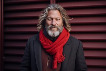 Portrait of a handsome senior man with long gray hair, wearing a red scarf and coat, standing outdoors on a winter day. - Powered by Adobe