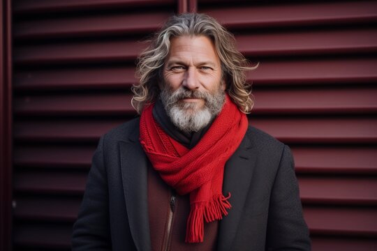Portrait of a handsome senior man with long gray hair, wearing a red scarf and coat, standing outdoors on a winter day.
