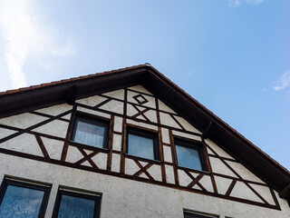 Facade of an old half timbered building. The traditional construction method used wooden beams and plaster material. Exterior wall with windows and the roof from a low angle.