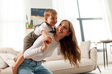 mother plays and rejoices with her little son at home, a young woman lifts her child up and laughs together