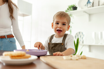 funny little boy eats milk breakfast in the kitchen and looks at the camera with an open mouth