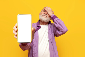 Confused old bald grandfather shows facepalm and blank smartphone screen on yellow isolated...