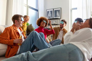 Naklejka premium multiracial group of young student friends playing charades together and drinking beer at party at home