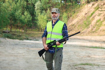 Fototapeta premium Man with hunting rifle wearing safety vest outdoors