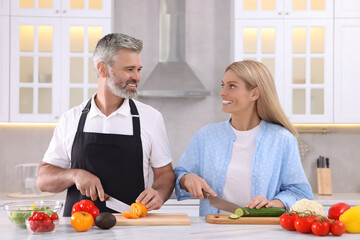 Happy affectionate couple cooking together at white table in kitchen