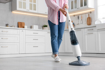 Woman cleaning floor with steam mop in kitchen at home, closeup