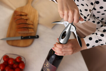 Romantic dinner. Woman opening wine bottle with corkscrew at table, closeup