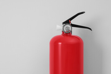 Fire extinguisher near light grey wall, space for text