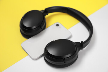 Modern wireless headphones and smartphone on color background