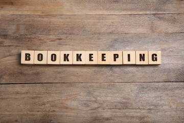 Word Bookkeeping made of cubes with letters on wooden table, flat lay