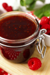 Jar of delicious raspberry jam and fresh berries on board, closeup