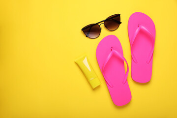 Stylish pink flip flops, sunscreen and sunglasses on yellow background, flat lay. Space for text