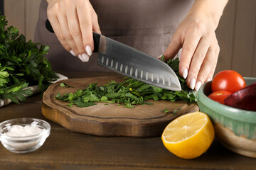 Woman cutting fresh parsley at wooden table, closeup