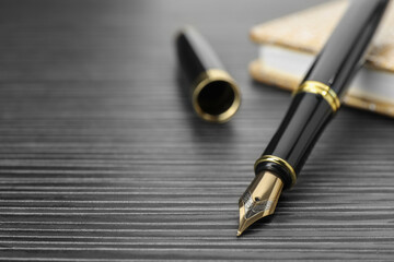 Stylish fountain pen and notebook on black wooden table, closeup. Space for text