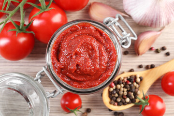 Jar of tasty tomato paste and ingredients on wooden table, flat lay