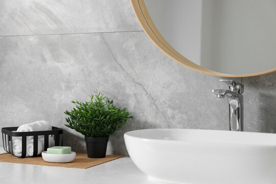 Potted artificial plants, rolled towels and soap near sink on bathroom vanity