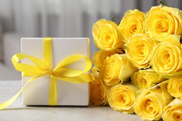 Beautiful bouquet of yellow roses and gift box on light grey table, closeup