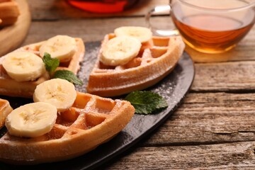 Tasty Belgian waffles with banana and mint on wooden table, closeup. Space for text