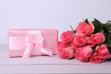 Gift box with pink bow and bouquet of beautiful roses on white wooden table