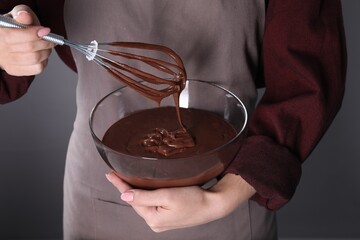 Woman with whisk making chocolate cream on grey background, closeup