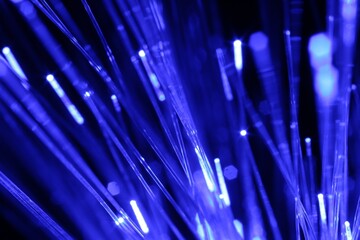 Optical fiber strands transmitting blue light on black background, macro view