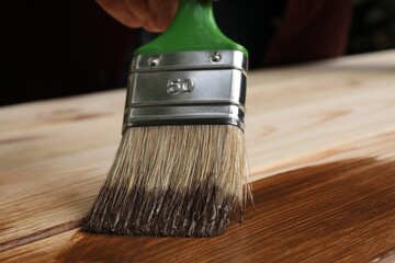 Man applying wood stain onto wooden surface, closeup