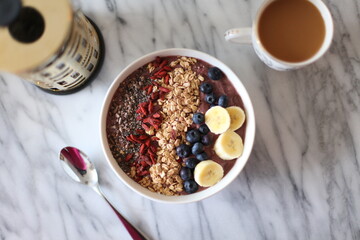 Top down view of a healthy açaí smoothie bowl topped with fresh fruit and granola served with a cup of coffee.