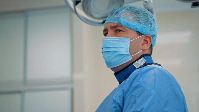 Serious concentrated male surgeon in mask and cap. Doctor wearing protective suit from x-rays is focused on the screen.