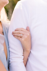 A close-up of a woman's arm as she clutches her fiance's arm. He wears a white shirt.