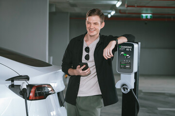 Young man travel with EV electric car to shopping center parking lot charging in downtown city...
