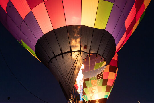 Hot air balloons glowing in the night as the pilot ignites the burner to fill the balloon's envelope with hot air..