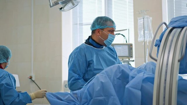 Doctor performing surgery is focused on the screen in front of him. Surgeon carries out endoscopic operation assisted by nurse.