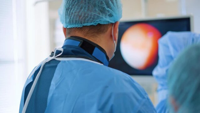 Rear view of a surgeon wearing x-ray protective collar. Operating doctor looking at the screen performing endoscopy. Blurred backdrop.