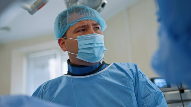 Caucasian male surgeon in x-ray protective suit, mask, cap and coat performing operation. Doctor performs endoscopy. Low angle view.