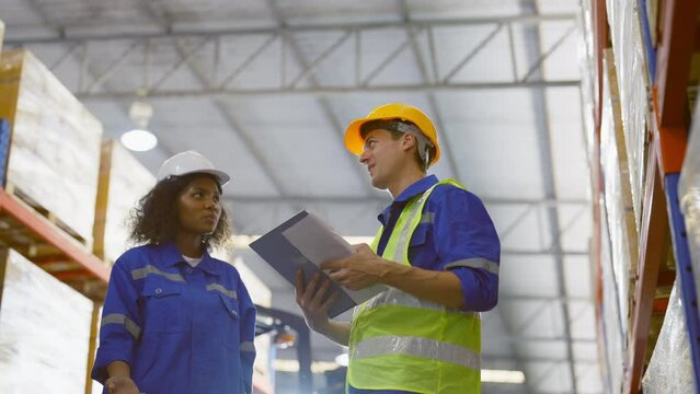 Smiling workers in distribution warehouse having a cheerful conversation. They wearing vest and safety helmet in work