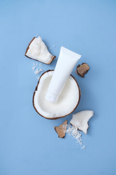 A tube of unlabeled facial cleanser is placed inside half a coconut on a blue background. View from above. Coconut water contains cytokinin, which helps fight skin aging.